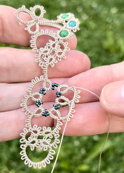 Tatting a lace necklace with ecru thread and green beads.