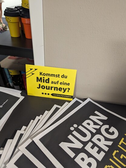 Postkarte im gelben Design des Nürnberg digital Festival mit der Aufschrift "kommst du mid auf eine Journey? In Anspielung auf Bildgenerierung mittels midjourney.