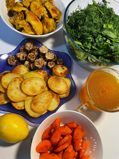 A picture of all the ingredients in this dish: Upside Down Chicken. Top left, clockwise: roasted boneless chicken thighs, the greens (spinach, dill, chives), home made chicken stock from boiling the chicken first before browning, roasted carrots sliced on the diagonal, a whole lemon, and a blue plate with roasted eggplant and golden Yukon Gold potatoes. 
