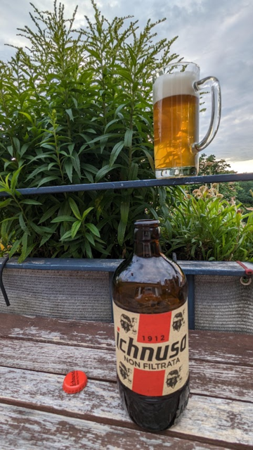 Eine Flasche Ichnusa-Bier auf einem Tisch im Freien. Über dem Bier auf einem Geländer ein Glas mit Bier vor einer Pflanze.