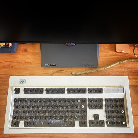 IBM Model M frame without keycaps with a lot of dirt and dust on a desk. Background: hard disk, Asus display, iPhone dock.
