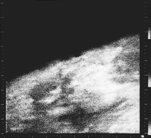A grainy, blotchy, black and white photo of Mars. It covers a bit more than half the photo, arcing up from the lower left to upper right of the photo.