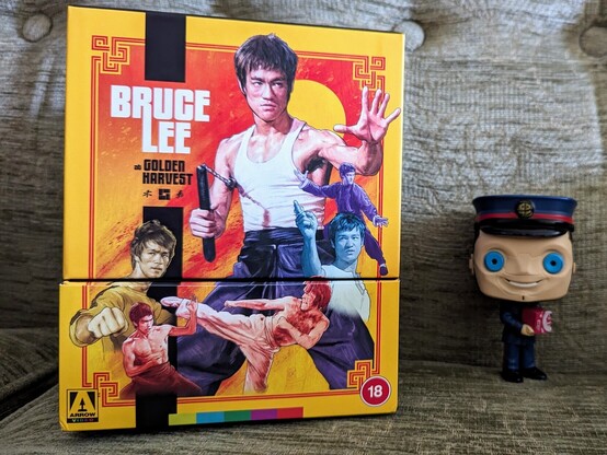 The Kerblam Man figure from Doctor Who standing next to the new 4K set Bruce Lee at Golden Harvest by Arrow Video, containing all of Lee's feature films.