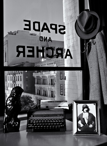 Window from the Dashiell Hammett Suite in the Hotel Union Square in San Francisco, the hotel Hammett first stayed in with his wife when he came to town. A black statue of a falcon (the Maltese Falcon), a typewriter and a photo of a woman (likely Lillian Hellman) are on the shelf in front of the window. SPADE and ARCHER is painted in block letters on the glass.