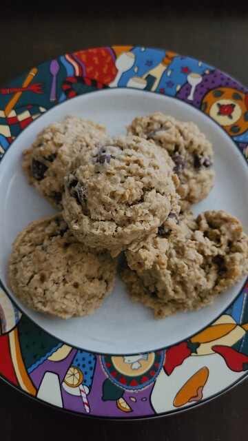 A colorful plate with five oatmeal dark chocolate covered raisin cookies sitting in a small mound.