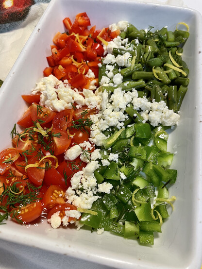 Before baking - the chopped veggies as described sitting in a white rectangular baking dish, covered with bits of feta cheese, fresh dill, and lemon zest.
