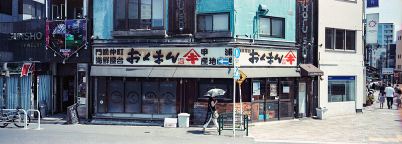 A woman carrying an umbrella under a hot sun in Tokyo; with Fujifilm Reala 100 and Fujifilm TX-1.