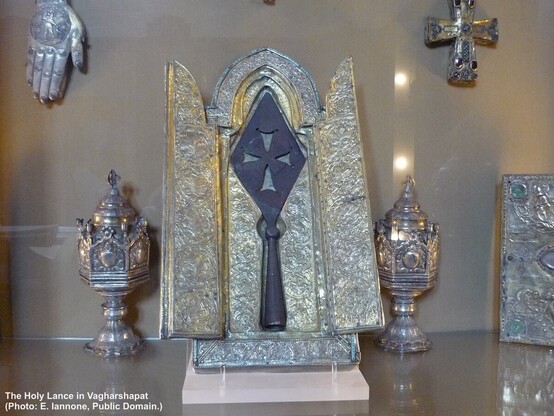 Photo of a rhombic spear tip with cross shape cut into its blade, presented in an open reliquary.