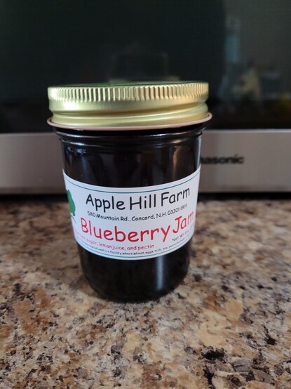 A jar of blueberry jam on a brown counter. The label shows the local farm it came from.