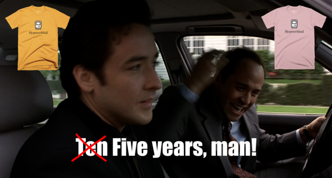 The scene in Grosse Pointe Blank where John Cusack and Jeremy Piven are in a car, and Piven can’t believe Cusack has been gone for “Ten years, man!” In the subtitle text, the word “Ten” is crossed out with a red “X” and “Five” is written in its place. A gold Hypercritical t-shirt and a pink Hypercritical t-shirt appear in the upper left and right corners of the frame.