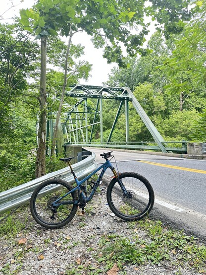 Mountain bike leaning on a guardrail with a green box girder bridge and roadway in the background.