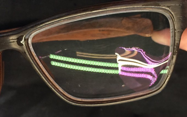 Photo of glasses with anti-reflection coating. In the glasses the reflection of a white LED light strip appears green. On the glasses are also water droplets. There the reflected light turns pink, due to different boundary effects at the air/water-coating interface.