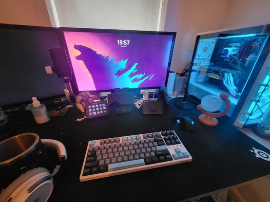 A computer setup with two monitors showing a godzilla image, a grey with some blue accents on the keyboard, a mouse, a pc tower with blue light from fans, and led strips.