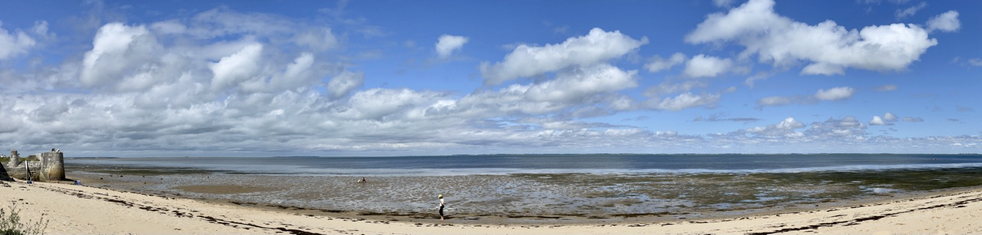 Photo panoramique de la plage juste à côté des remparts. La marée est basse, le ciel est bleu avec des nouages dodus blancs et gris