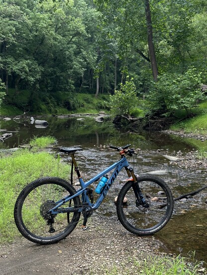 Mountain bike propped up on a stick in front of a small creek in a clearing in the woods.
