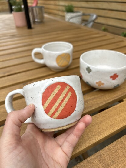 a coffee cup with red underglaze in front of a few other handmade pots 