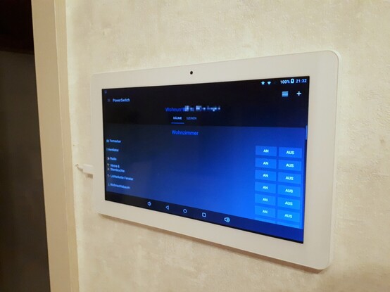 A white android tablet in which two small holes are bored on the back and hung on the wall with two nails. On the screen is the app "PowerSwitch" open in darkmode. On the left side of the tablet is a microUSB plug, the cable comes out of the wall and is routed in the door frame. 

In the white door frame is a closed glass door which actually does not matter at all because it does not belong to the topic, I just wanted to mention it in case someone asks about it.

The wallpaper in the background is white-gray and should represent a kind of concrete pattern.