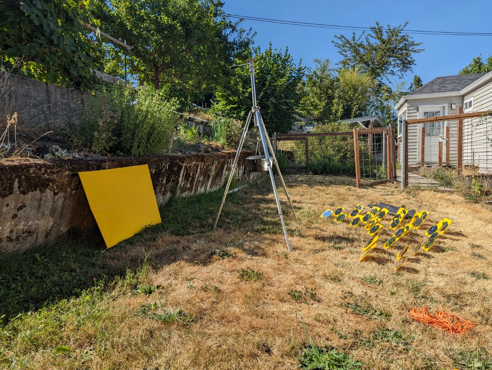 The tripod is holding a cast iron dutch oven and there are 32 small mirrors reflecting the sun towards it. There is a yellow sheet of coroplast. The mirrors are controlled by bamboo skewers driven into the ground.