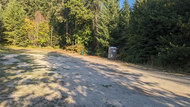 View of the parking lot at the base of Antoine Peak. You can see long tree shadows stretching across and a port a potty before the path to the trailhead. Not pictured is the well stocked hand sanitizer inside.