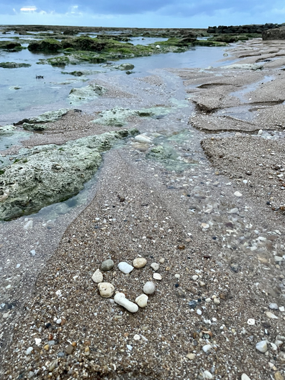 Hart made of small beach stones laying on the sand. It is a rainy late evening and we can see dark grey clouds at horizon. 