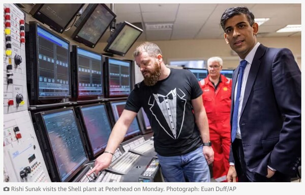 photo of Rishi Sunak visiting an industrial plant control room, standing next to a man wearing a t-shirt with a tux print design.