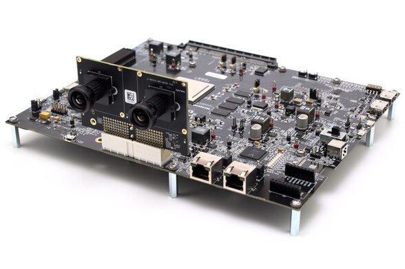 An angled photo of the entire Microchip PolarFire SoC Video Kit development board, against a white background. The black PCB is turned with two Ethernet ports facing the camera, and a daughterboard connected with two wide-angle camera lenses sticking out like a bug's eyes.