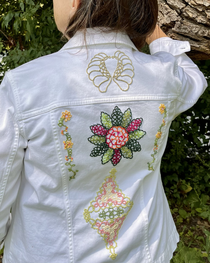 White jeans jacket back embellished with angel wings design and colorful floral designs.