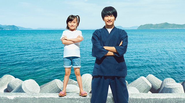 The promotional picture for Japanese series #Barakamon shows little Naru, a girl with a side ponytail, and a summery outfit, standing on the jetty of her village, crossing her arms with a self-confident expression. Standing next to her is calligrapher Seishuu, also crossing his arms. Since she's standing on a cement breakwater, she's almost as tall as him ! Behind them is a cyan-colored ocean, with some islands appearing faintly in the distance.