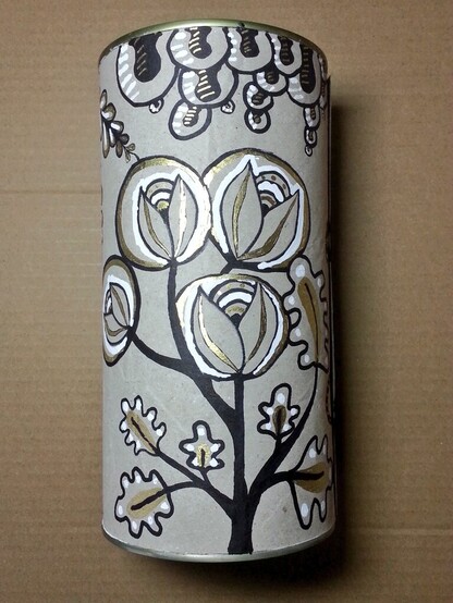 Sur un fond gris de papier recyclé une boîte cylindrique est entouré d'un papier recyclé décoré avec un motif végétal en noir blanc et or.

Ce sont des sortes de fleurs extravagantes et imaginaires, un peu naïves, avec des feuilles rayées de blanc et des tiges noires. 

Le doré sur la boîte va bien avec le métal de la boîte elle-même qui est transparaît en haut là où le couvercle plastique doit se fermer. Et le couvercle n'est pas présent à l'image. 

Le tout forme un kit de crochet décoré, et a été garni comme indiqué dans le post. 