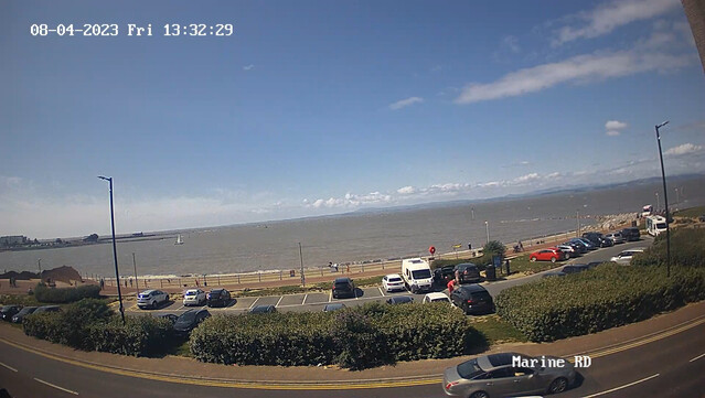 Soft waves lapping the shore beyond a car park on a sunny day.