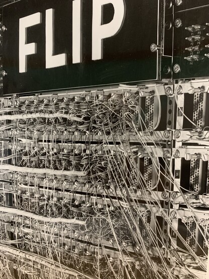 Black and white vertical oriented image with white on black FLIP lettering at the top on the left hand side and the 
And the Floating Indexed Point (FLIP) back panel w/ very extensive wiring and a register display below the signage. This is largely gray, silver and white in the image. 