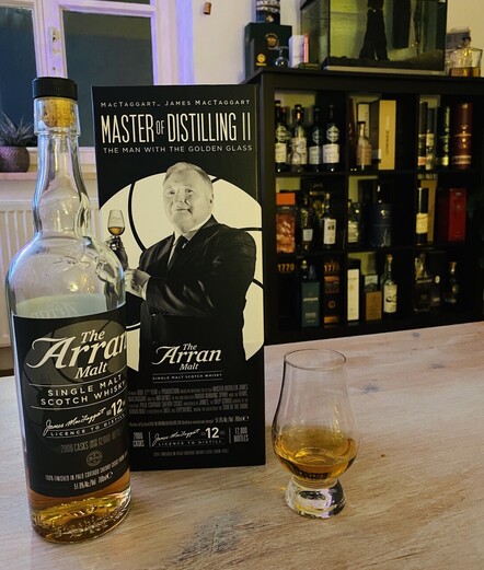 Whiskyflasche mit eingeschenktem Dram vor Whiskyregal. Verpackung im James Bond Filmdesign. 
