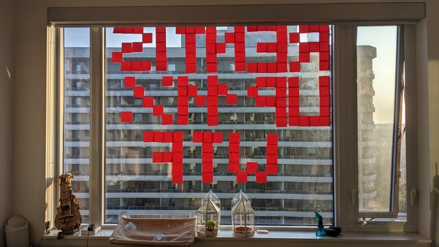 An apartment window. A bunch of red post-it's spells out "Rent is up 11% WTF" mirrored 