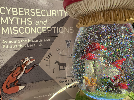 A copy of the book  Cybersecurity Myths and Misconceptions: Avoiding the Hazards and Pitfalls that Derail Us next to a gnome is a globe full of sparkling glitter.