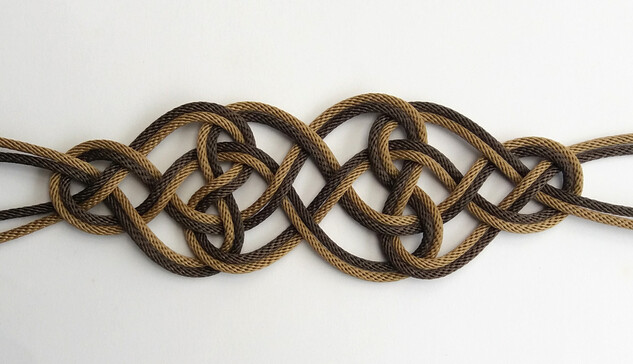Nœud de forme globalement allongée.
Les croisements des fils se font alternativement dessus-dessous.
Le motif du centre du nœud, faisant à peu près la moitié de la longueur, est formé par deux groupes de deux fils se croisant.
Les fils forment des vagues.
Ce motif est entrelacé avec deux motifs de chaque côté, chacun faisant un quart de la longueur.
Ce deuxième motif fait penser à une forme de cœur, dont la pointe, ici formée par une petite boucle, serait tournée vers l'extérieur du nœud.
Les fils ayant servi a tisser le nœud ressortent par les petites boucles aux extrémités.
Le nœud est doublé : un premier passage est réalisé avec une cordelette de couleur beige, un second avec une cordelette de couleur marron foncé.