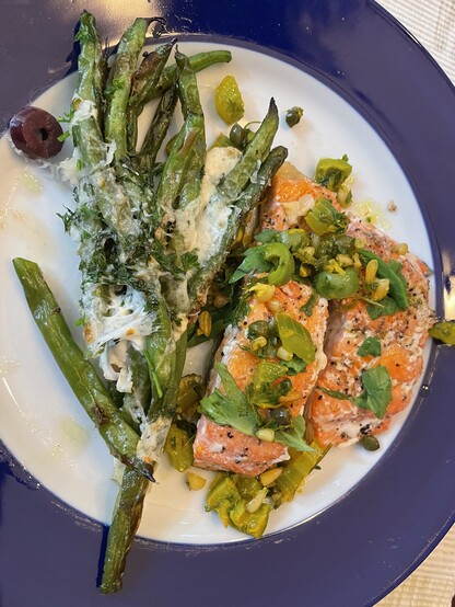 A blue-rimmed dinner plate with roasted green beans, parmesan cheese and kalamata olives on the left, next to Alaskan salmon with a celery-caper and pine nut topping.
