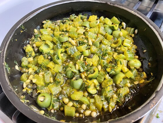 A large saucepan on the stove cooking green olives, minced celery, parsley, capers and pine nuts to be served over Alaskan salmon.
