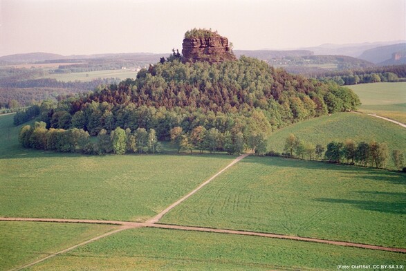 Foto eines kleinen Tafelbergs mit steilen Hängen, der auf einem bewaldeten Hügel thront.