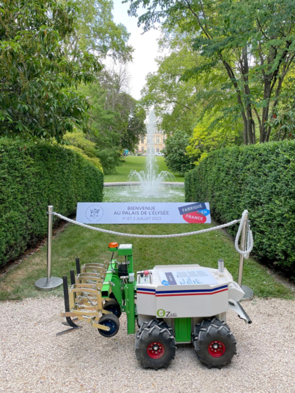 Photo d'un robot agricole Oz orné d'une bannière bleu blanc rouge, dans les jardins du palais de l’Élysée.