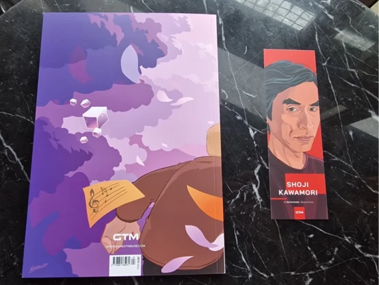 Foto de la revista GTM cuya contraportada está dedicada al juego Inner Ashes. Junto a la revista hay una marca páginas con una ilustración del rostro de Shoji Kawamori