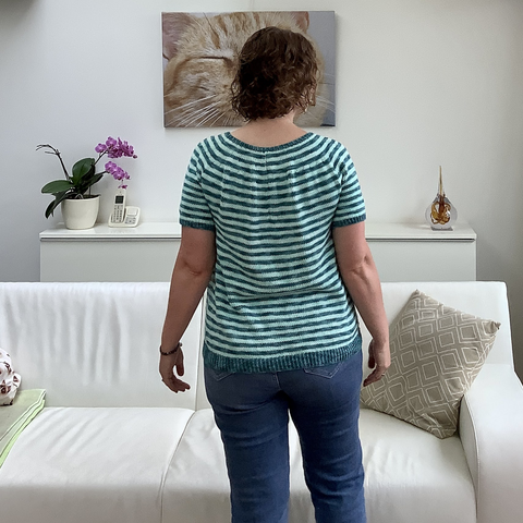 A woman with chin length curly hair is shown from the back, wearing a knit striped tee.