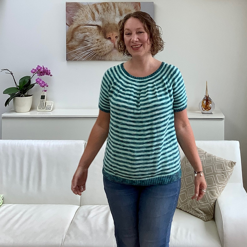 A woman with chin length curly hair smiles into the camera. She is wearing a knit striped tee.