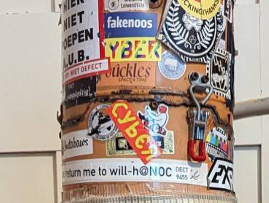 A close up of an orange gas canister covered in stickers. It is the top of the world o techno device