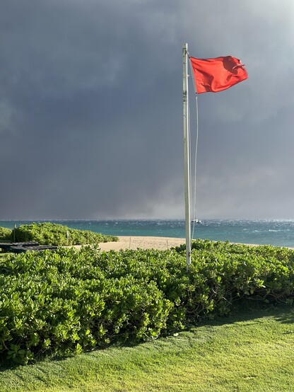 Picture of the Red Flag for the surf warning on Kaanapali Beach in Maui with smoke billowing behind it. 