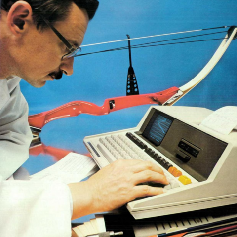 A man in a white coat using an early all-in-one desktop computer with a tiny monochrome screen.