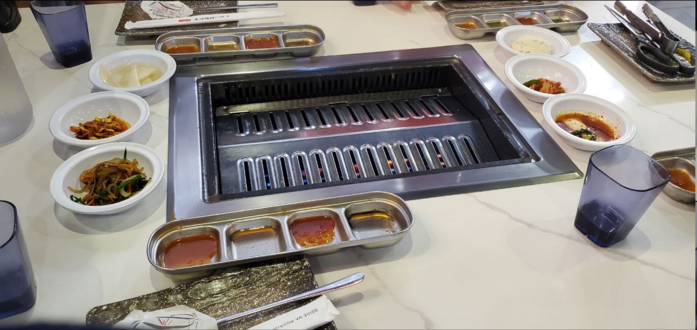 picture of a grill built into a table at a restuarant, surrounded by sauces and some sides
