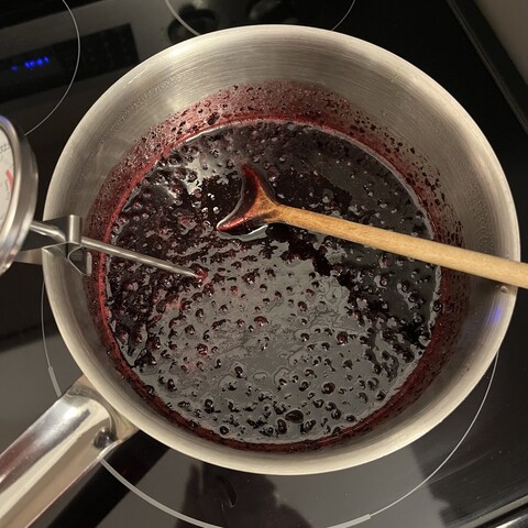 Currant mixture in a pot with a candy thermometer clipped to the side and a wooden spoon