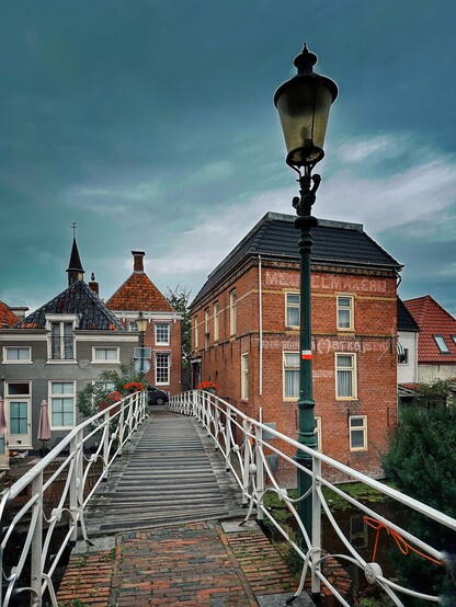 A pedestrian bridge with a street lamp lead towards several typical Dutch houses in the background. 