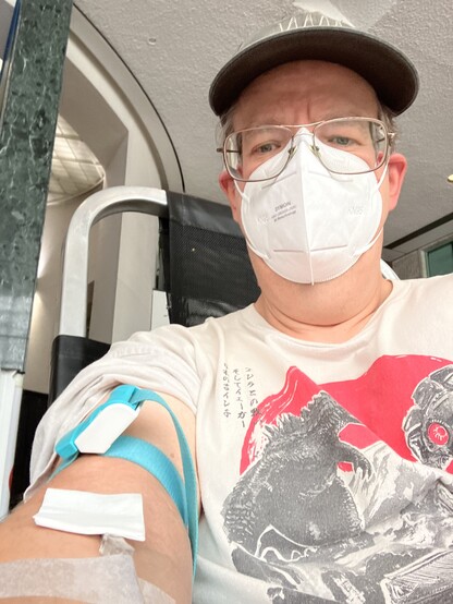 Selfie of me donating blood, white guy, baseball cap,  and a Godzilla tshirt.