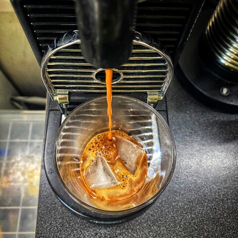 Drawing an espresso from an espresso machine into a glass over two ice cubes.